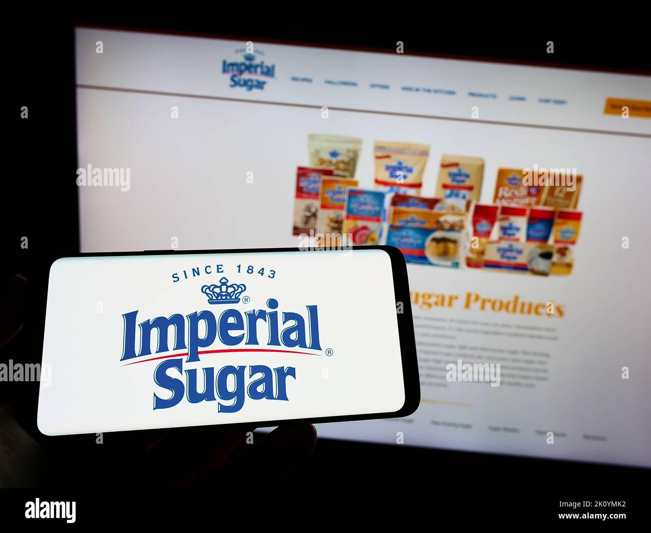 Personne tenant un téléphone portable avec le logo du producteur américain de sucre Imperial Sugar Company à l'écran en face de la page Web. Mise au point sur l'affichage du téléphone. Banque D'Images