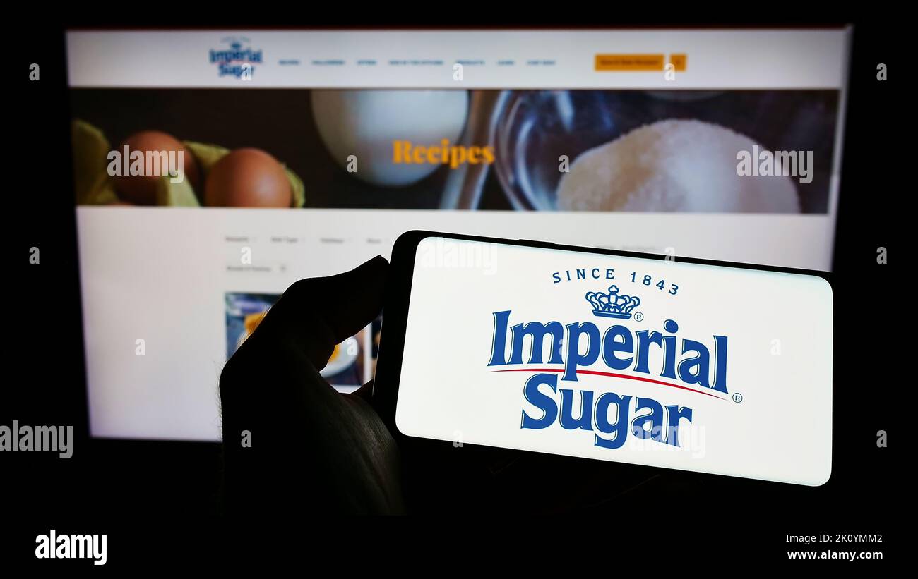 Personne tenant un téléphone portable avec le logo du producteur américain de sucre Imperial Sugar Company à l'écran devant la page Web d'affaires. Mise au point sur l'affichage du téléphone. Banque D'Images