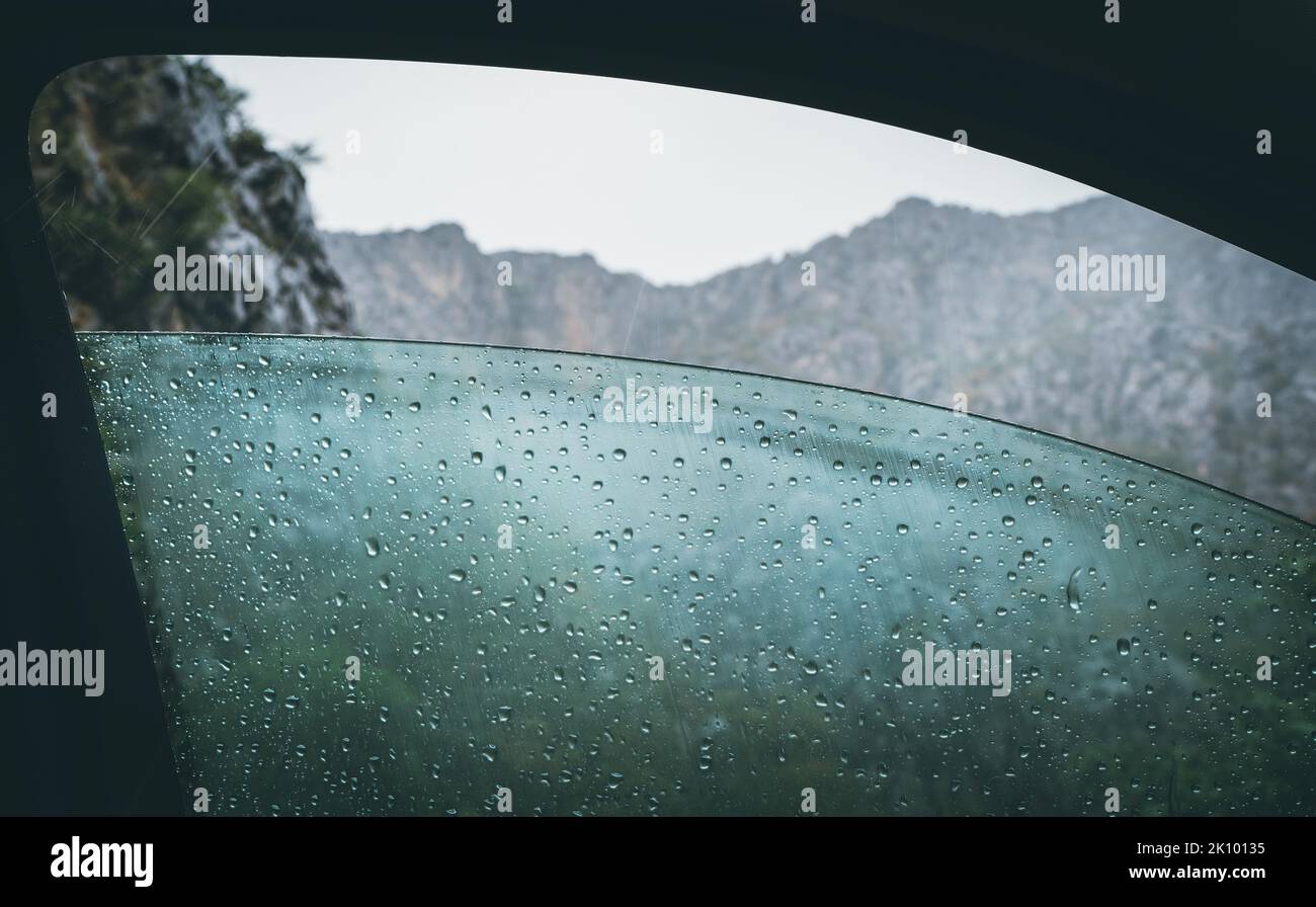 Porte de voiture avant à moitié ouverte fenêtre embuée couverte d'une pluie froide avec une chaîne de montagnes rocheuses et de lourds nuages orageux. Banque D'Images