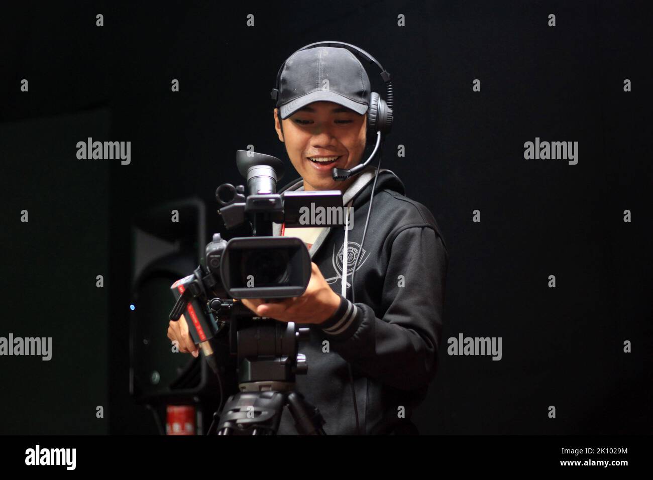 Caméraman souriant en utilisant l'appareil photo sur trépied en studio Banque D'Images