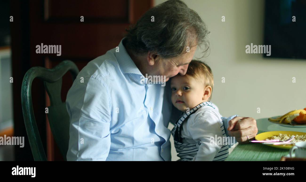 Grand-père tenant le petit-fils dans les bras à la table de repas. Grand-parent décontracté et franc avec bébé Banque D'Images