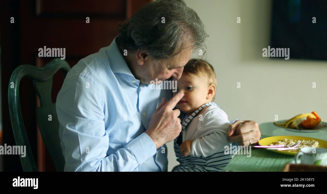 Grand-père tenant le petit-fils dans les bras à la table de repas. Grand-parent décontracté et franc avec bébé Banque D'Images