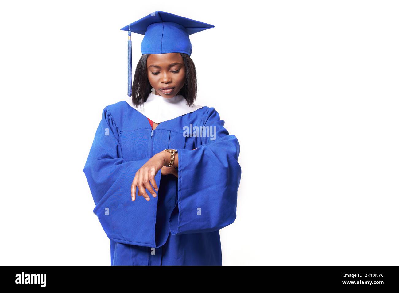 Une femme afro-américaine vêtue d'une robe bleue et d'un chapeau sur un fond blanc isolé regarde la montre sur sa main. Le concept de l'éducation, une étudiante de deuxième cycle. Photo de haute qualité Banque D'Images