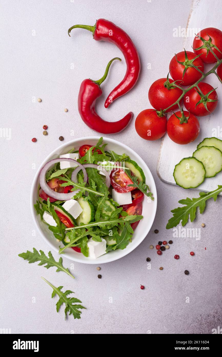 Vue de dessus de la nourriture végétarienne saine et savoureuse. Salade de feuilles d'arugula fraîches, tomates cerises, fromage doux et concombre sur fond de béton gris Banque D'Images