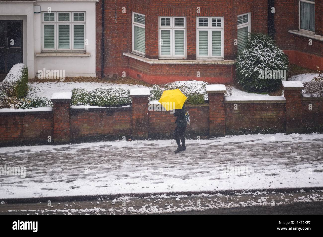Un piéton avec un parapluie jaune marchant dans la rue London dans la neige d'hiver Banque D'Images