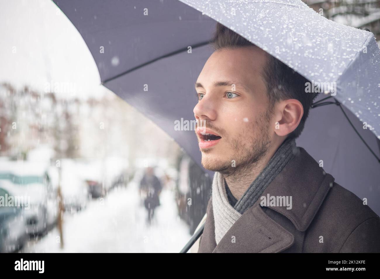 Portrait d'un beau jeune homme avec un parapluie respirant de l'air chaud dans la neige d'hiver Banque D'Images