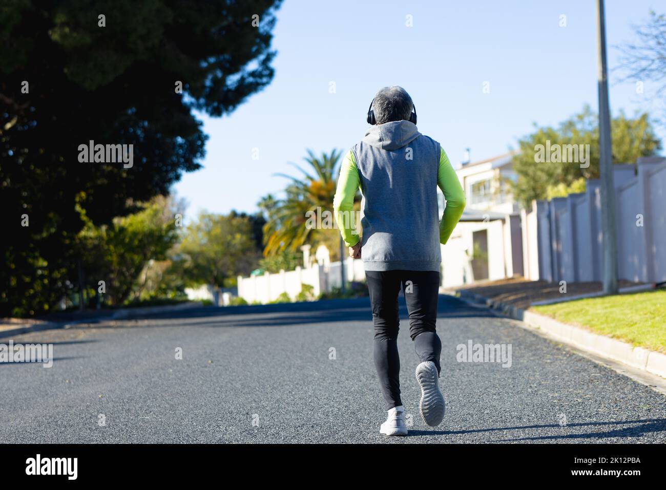 Vue arrière de l'homme biracial senior en vêtements de sport et casque de jogging sur route ensoleillée Banque D'Images