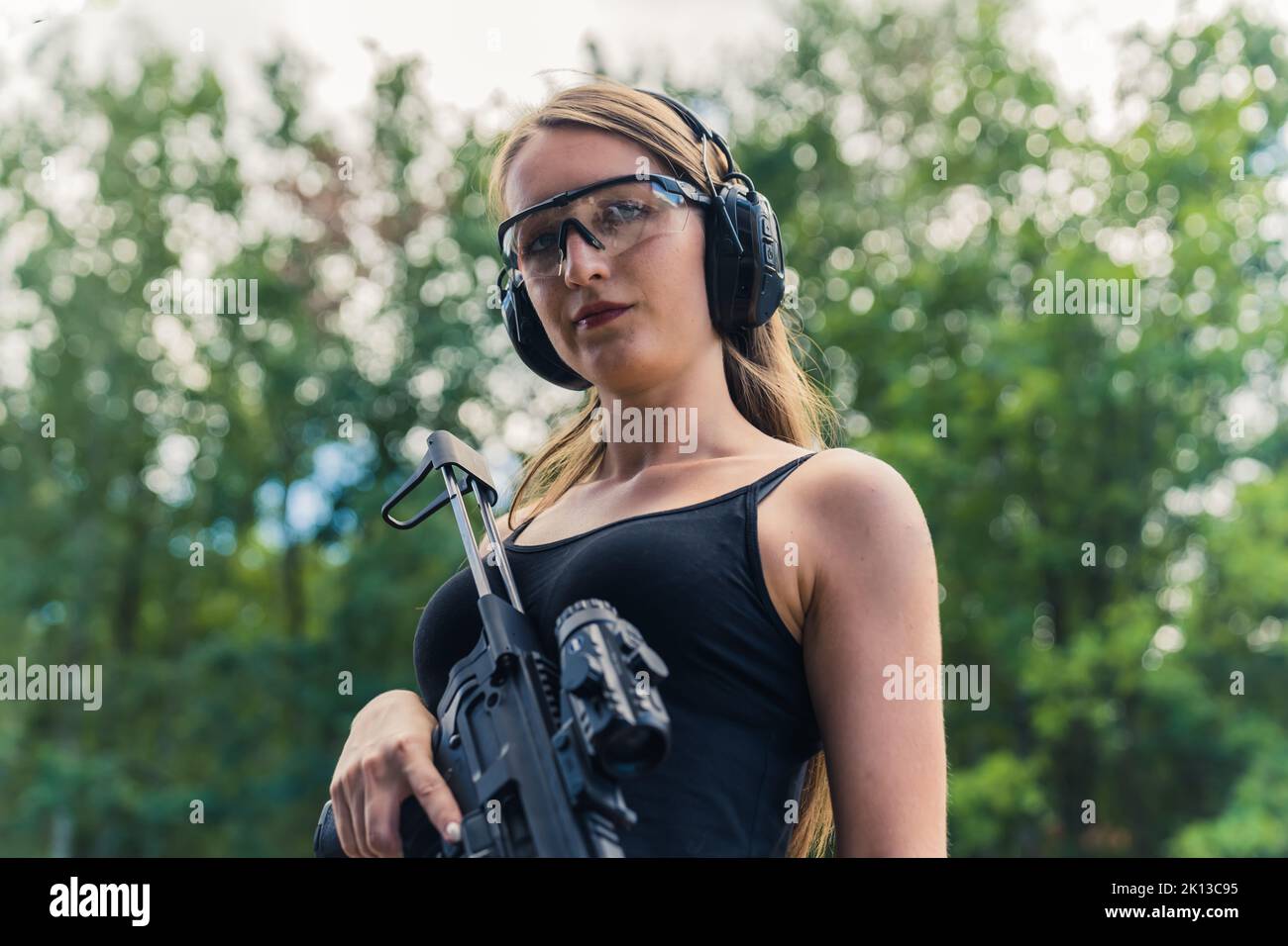 Confiante caise fille avec lunettes de protection et casque tenant une carabine à portée de tir, tir moyen. Photo de haute qualité Banque D'Images