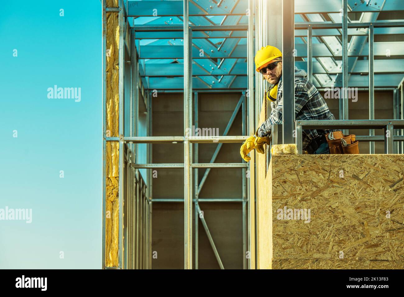 Entrepreneur caucasien d'âge moyen professionnel debout sur le dessus de couvert avec des panneaux de bois structure de maison en acier. Ciel bleu clair dans le bac Banque D'Images