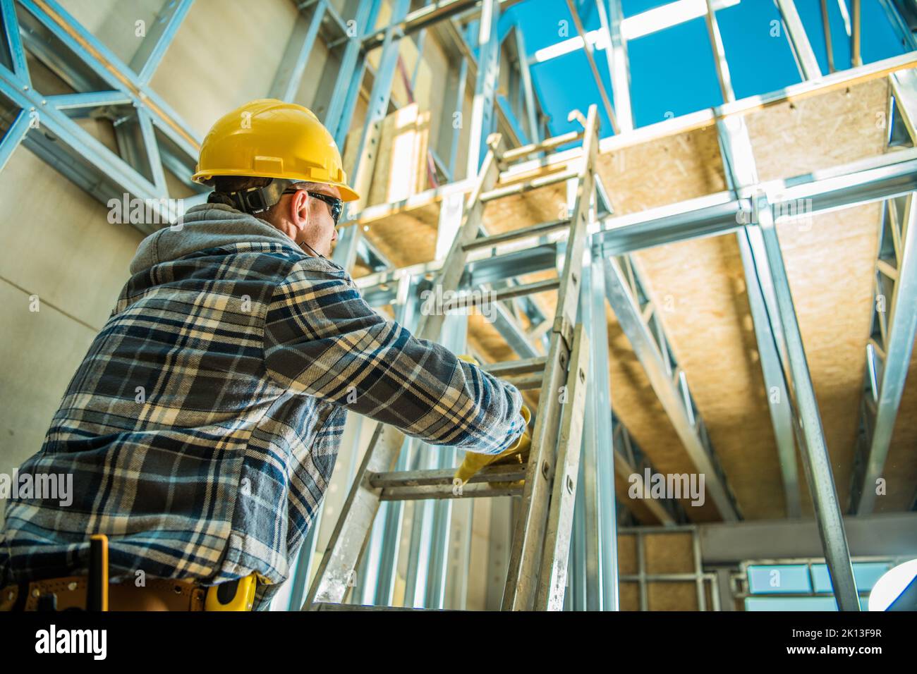 Vue de dessous photo d'un ouvrier de construction professionnel portant un casque de sécurité jaune grimpant l'échelle d'extension pour atteindre le prochain étage à New Commer Banque D'Images