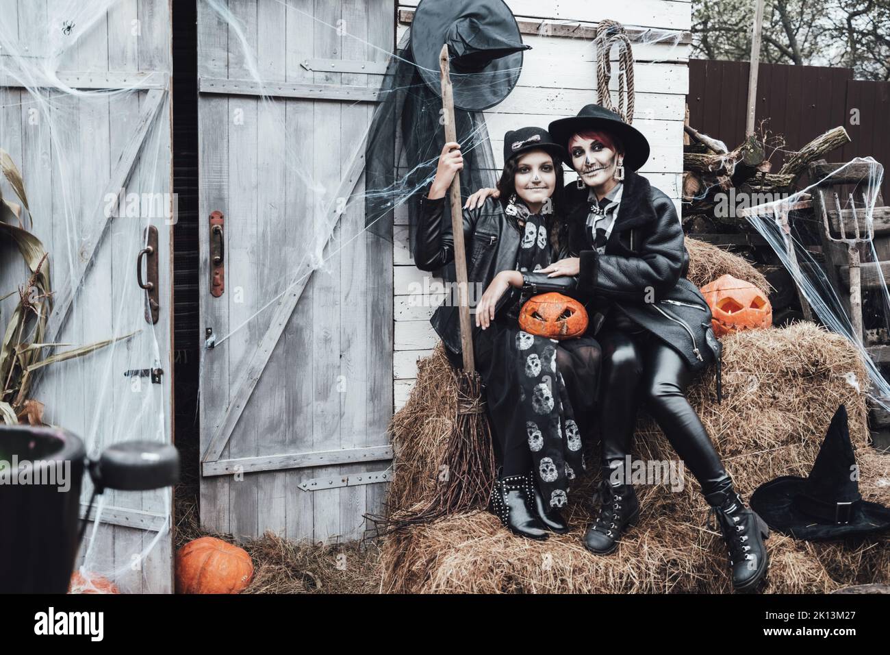 Famille, mère et fille effrayantes célébrant halloween. Grange de rue. Citrouille jack-o-lanterne.terrifiant crâne noir maquillage demi-visage et sorcières costumes, br Banque D'Images