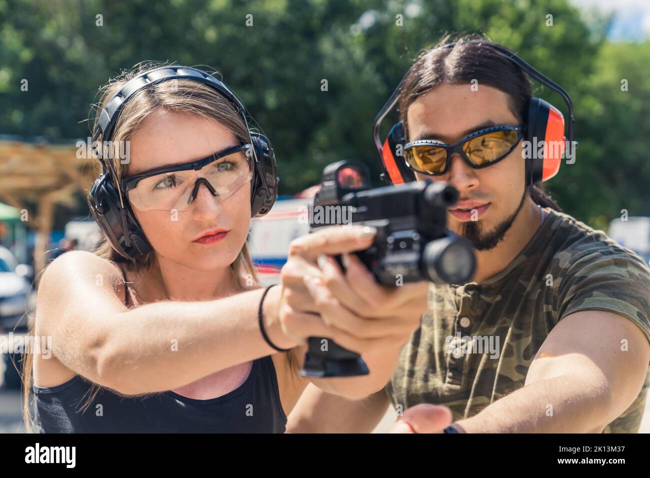 instructeur et fille avec casque et lunettes apprenant à utiliser un pistolet à la gamme extérieure, de gros plan moyen. Photo de haute qualité Banque D'Images