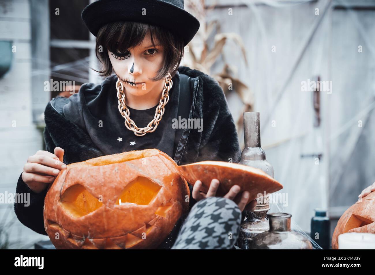 Belle petite fille effrayante célébrant halloween. Un maquillage noir et blanc terrifiant pour les demi-visages, un costume de sorcière, une image élégante. Amusez-vous à la fête des enfants en b Banque D'Images