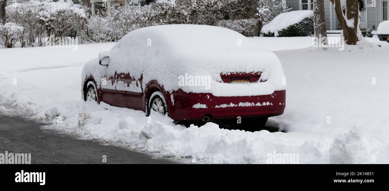Une voiture rouge couverte de neige garée dans la rue pendant une tempête, donc les chasse-neige ont dû se déplacer et bloquer la voiture. Banque D'Images