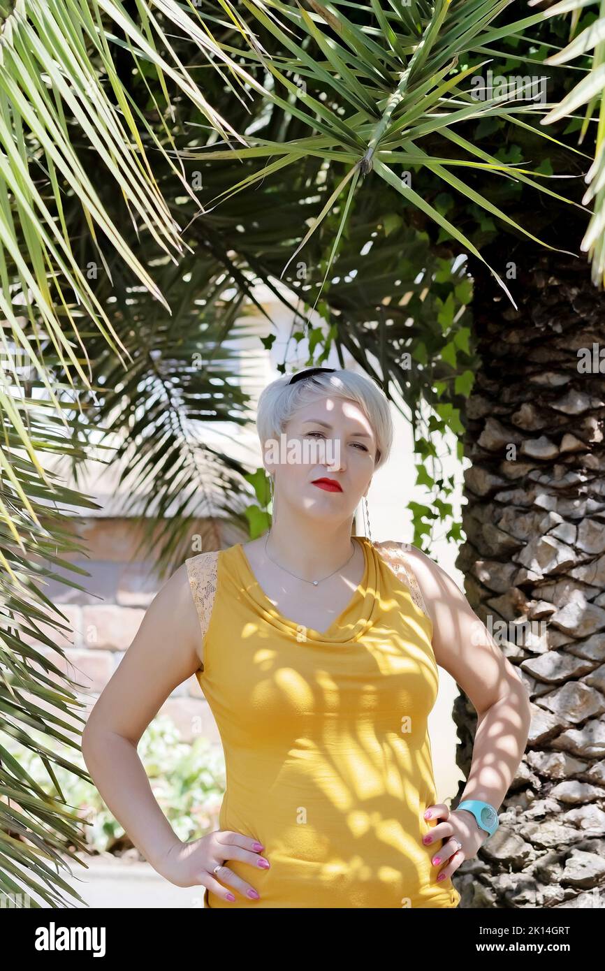 Belle femme blonde posant près du palmier dans le parc Banque D'Images