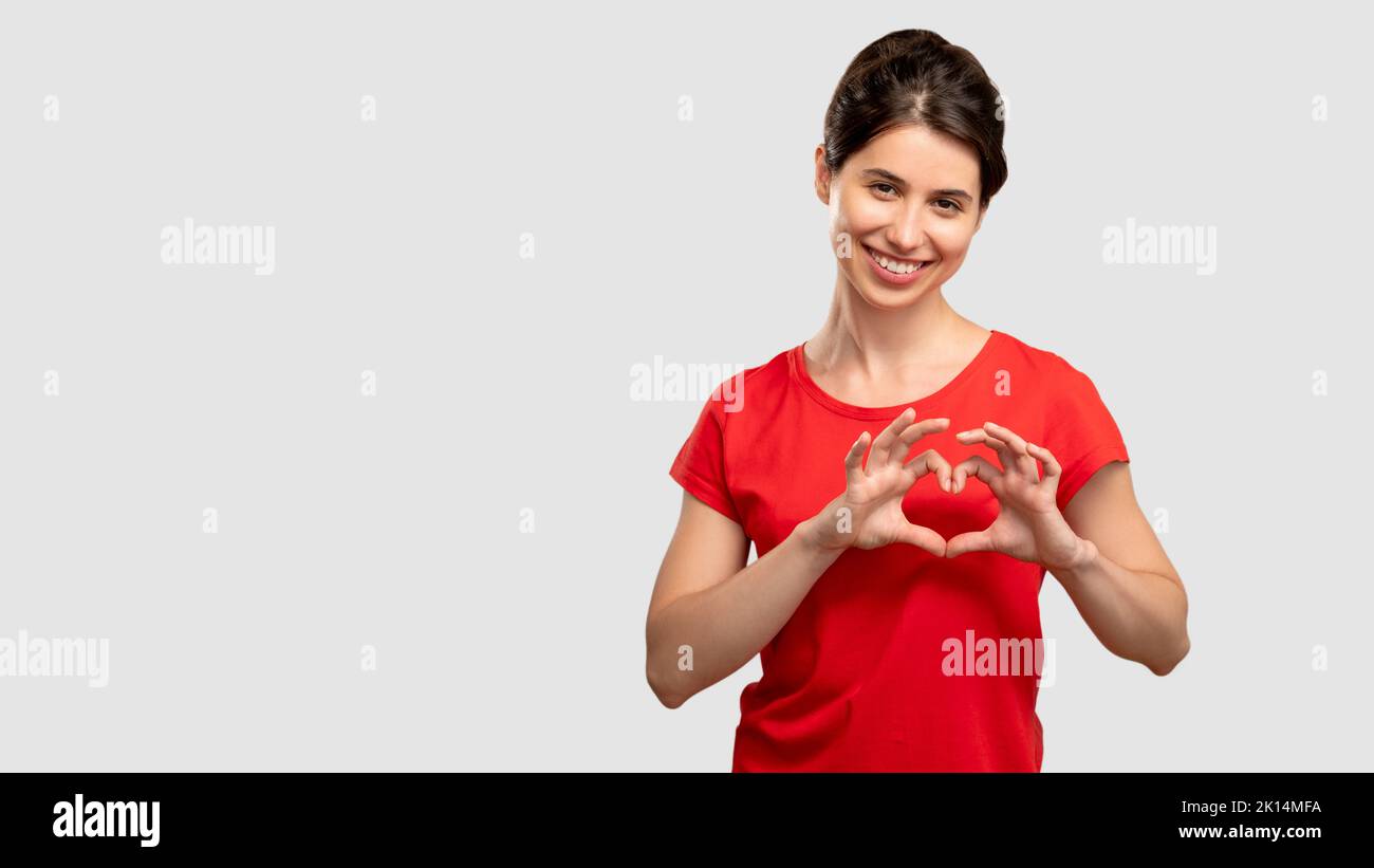 Geste du cœur. Envoyez l'amour. Bonne femme en t-shirt rouge regardant l'appareil photo. Isolé sur un espace de copie neutre. Affection et désir. Émotion romantique. Publicité Banque D'Images