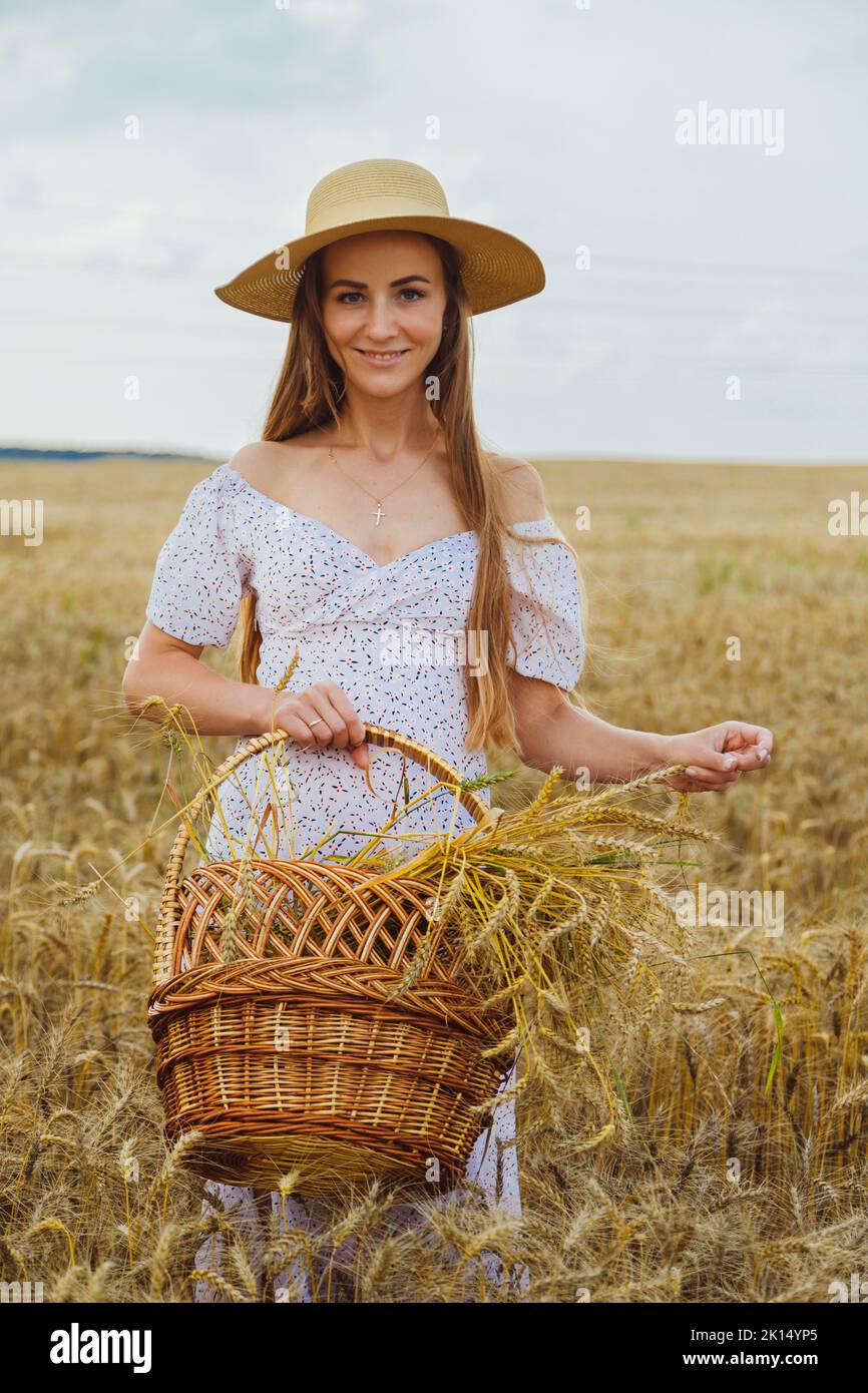 Jeune femme en chapeau au champ doré tenant le panier avec le seigle Banque D'Images