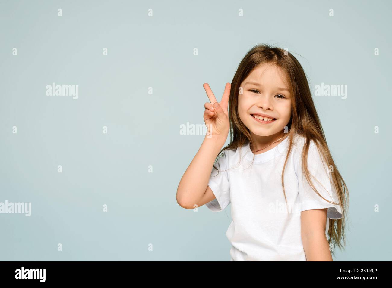 Bonne petite fille souriante montrant V signe de paix geste de main sur fond bleu. La paix au monde, arrêter la guerre. Banque D'Images