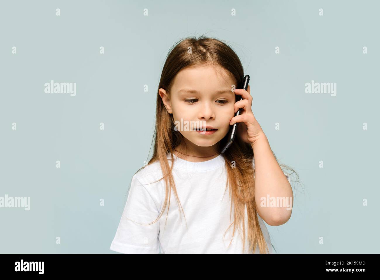 Mignonne caucasienne bébé fille parlant au téléphone, isolé dans le studio avec fond bleu, petite fille écoutant les nouvelles de maman. Banque D'Images