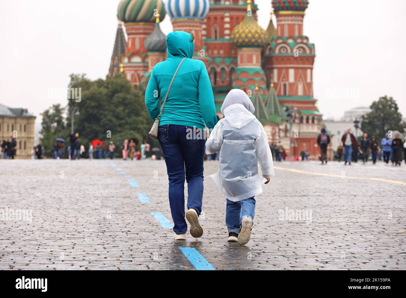 Pluie à Moscou, une femme avec un enfant en imperméable marche sur une place rouge sur fond de la cathédrale Saint-Basile. Temps pluvieux en automne Russie Banque D'Images