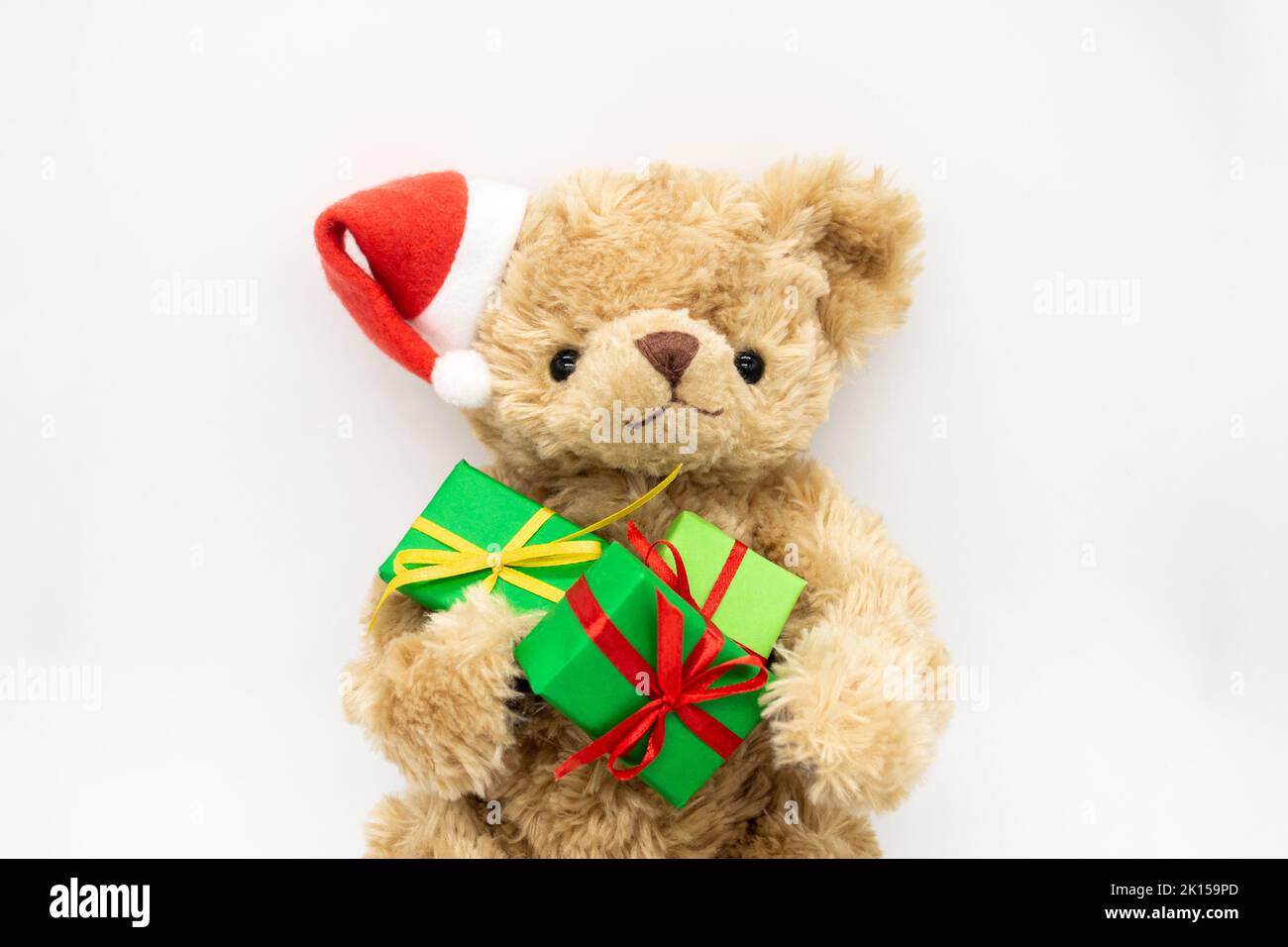 Un ours en peluche Teddy dans un chapeau de Père Noël rouge avec pompon sur une oreille, tenant des boîtes-cadeaux vertes dans ses pattes.Arrière-plan blanc, espace de copie.Le co Banque D'Images