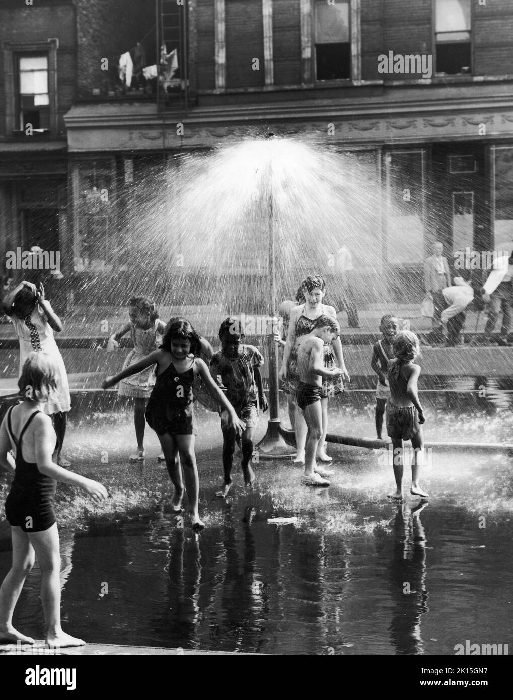 Les enfants se refroidissent sous une arroseur urbain dans la ville de New York, 1954. Banque D'Images