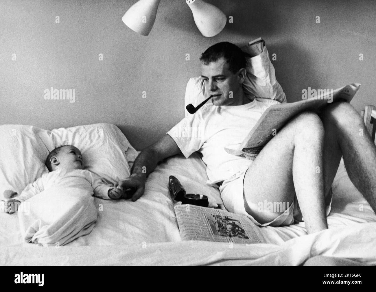Un père fume un tuyau près de son bébé de cinq mois à New York, en 1960. Banque D'Images