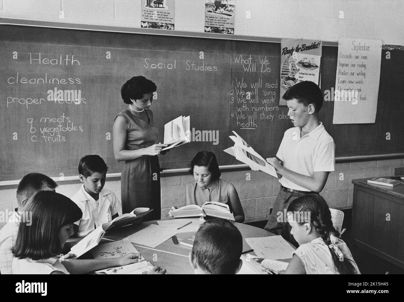 L'enseignant et les autres élèves d'une classe de cinquième année écoutent pendant qu'un jeune garçon lit à voix haute.Yonkers, Queens, New York.Vers les années 1950, 1960, Banque D'Images