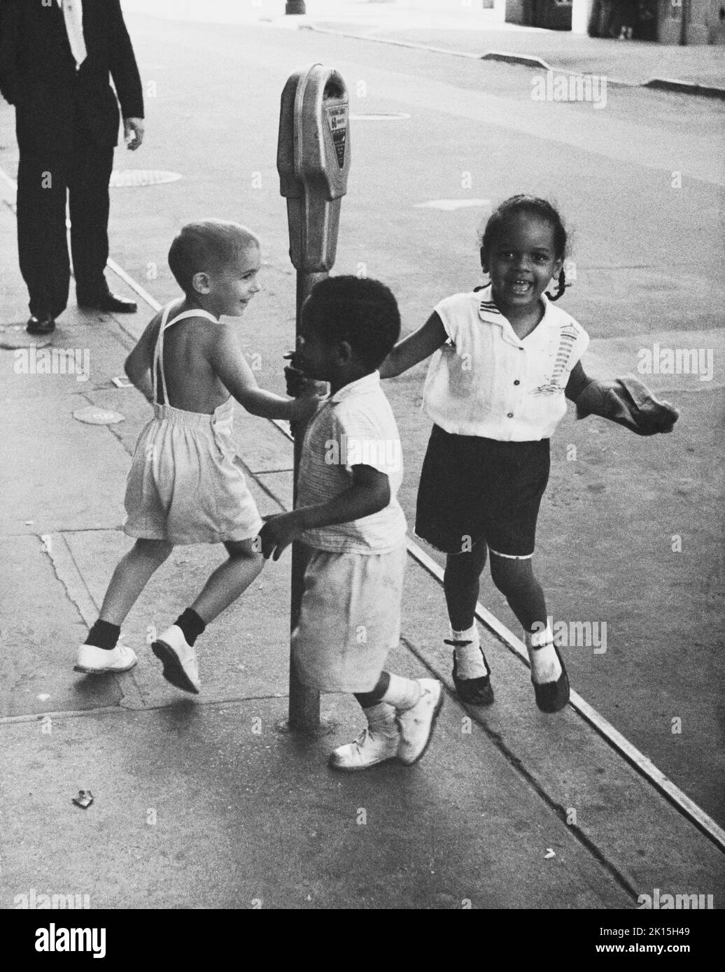 Trois enfants balancent un mètre de stationnement dans le Greenwich Village de New York.Vers les années 1960. Banque D'Images
