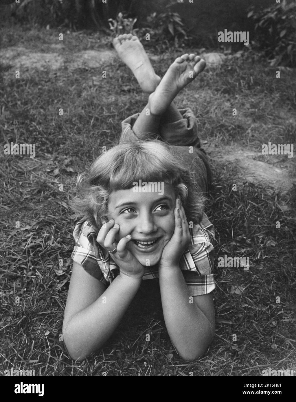 Une jeune fille pieds nus se détend dans l'herbe d'une cour. Banque D'Images