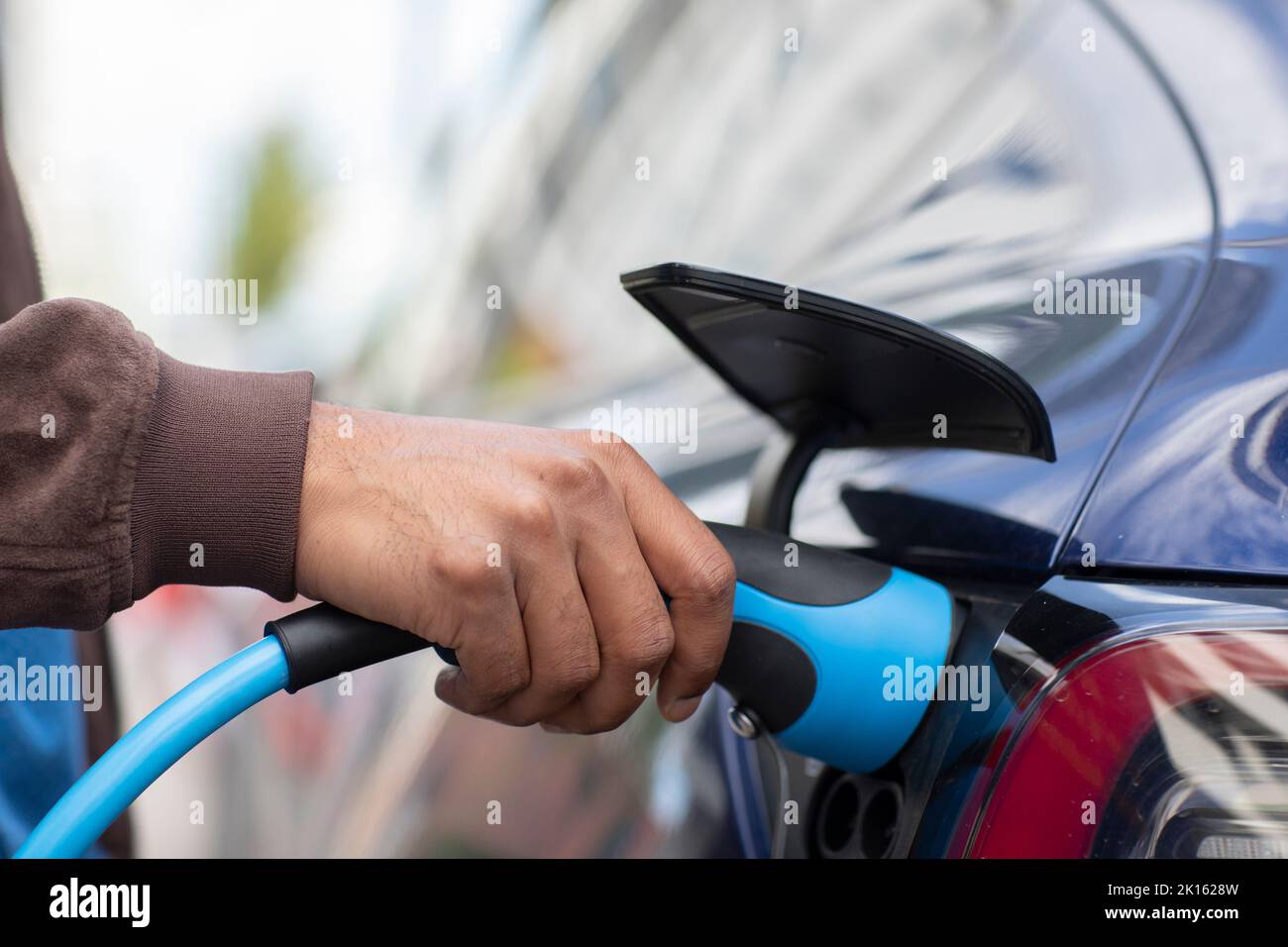 une main tenant le câble de charge à une station de charge Banque D'Images