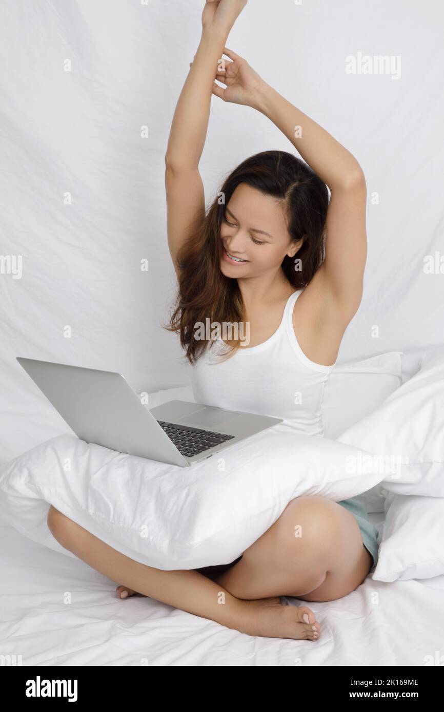 Femme asiatique travaillant sur un ordinateur dans un lit isolé sur blanc Banque D'Images