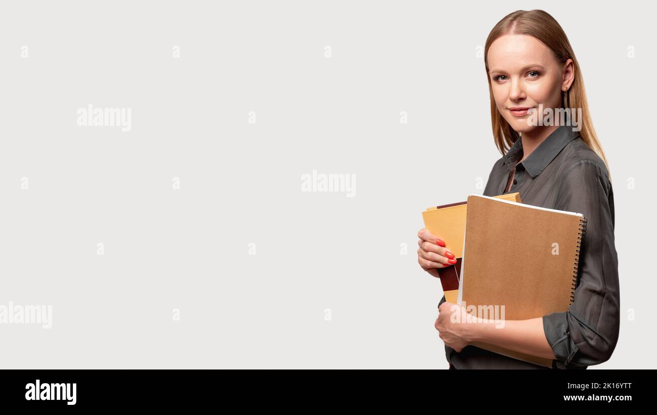 Femme intelligente. Mode de vie des enseignants. Enseignement à distance. Cours en ligne. Portrait d'une dame confiante en chemise grise debout avec des livres isolés sur la lumière neut Banque D'Images