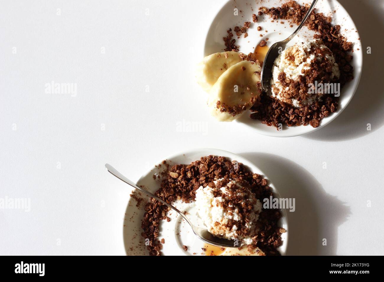 Petit déjeuner maison. Assiettes de fromage cottage avec granola, miel et banane sur fond de table blanche. Banque D'Images