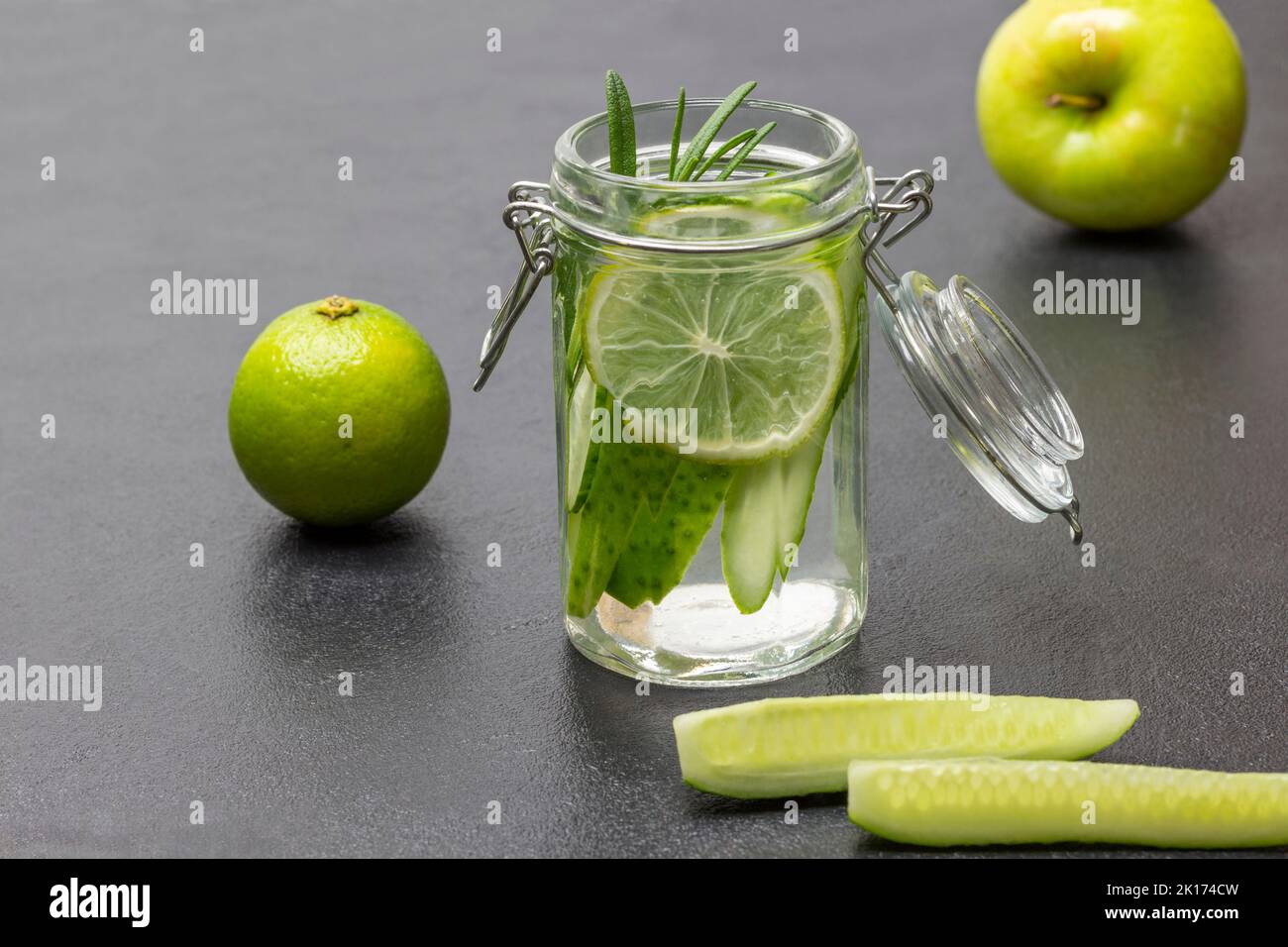 Boisson d'été avec citron vert et concombre dans un pot. Tranches de concombre sur la table. Citron vert et pomme sur table. Arrière-plan noir. Banque D'Images