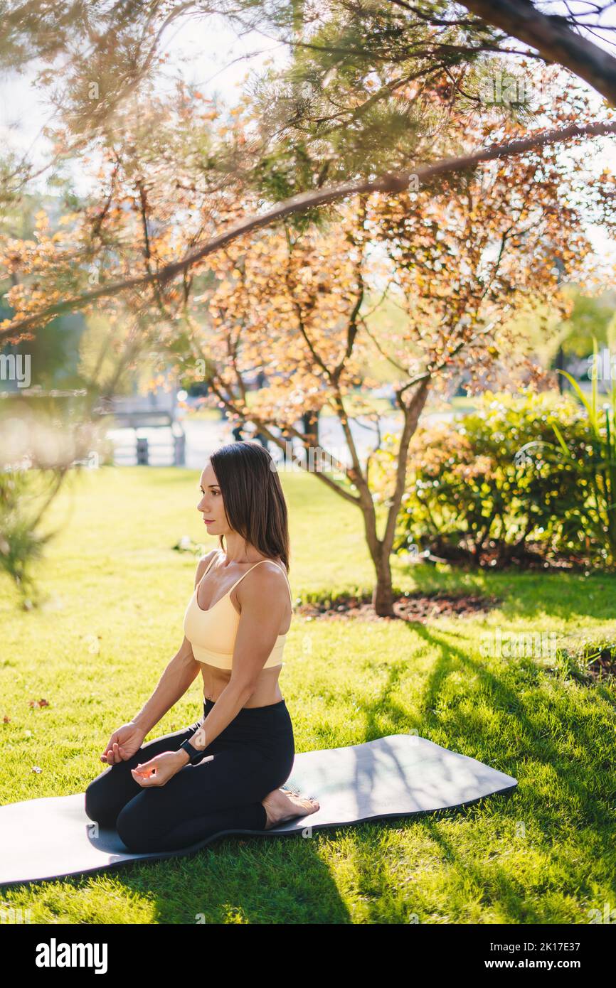 Femme s'agenouillant sur le tapis de yoga en attendant de commencer la procédure de méditation dans le parc le matin. Nature estivale. Nature verte. Actif sain Banque D'Images