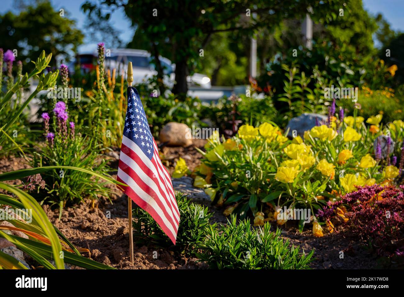 Le soleil du matin brille sur un drapeau américain qui se trouve dans un lit de fleurs sur le sentier Mariners entre Manitowoc et Two Rivers, Banque D'Images