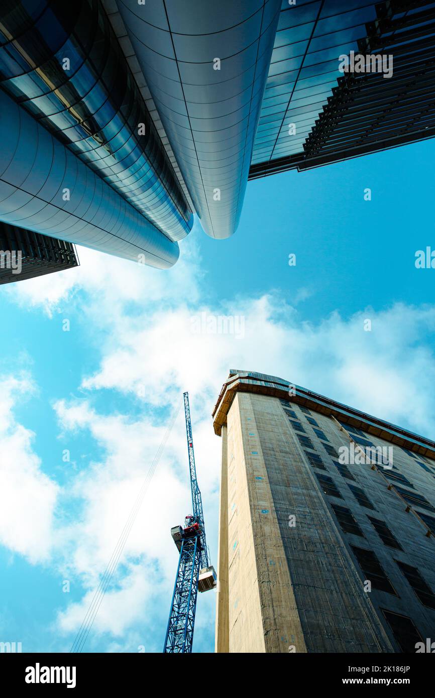 Une vue à angle bas qui donne sur un gratte-ciel en construction avec une grue entourée de bâtiments à façade de verre dans le centre-ville de Leeds Banque D'Images