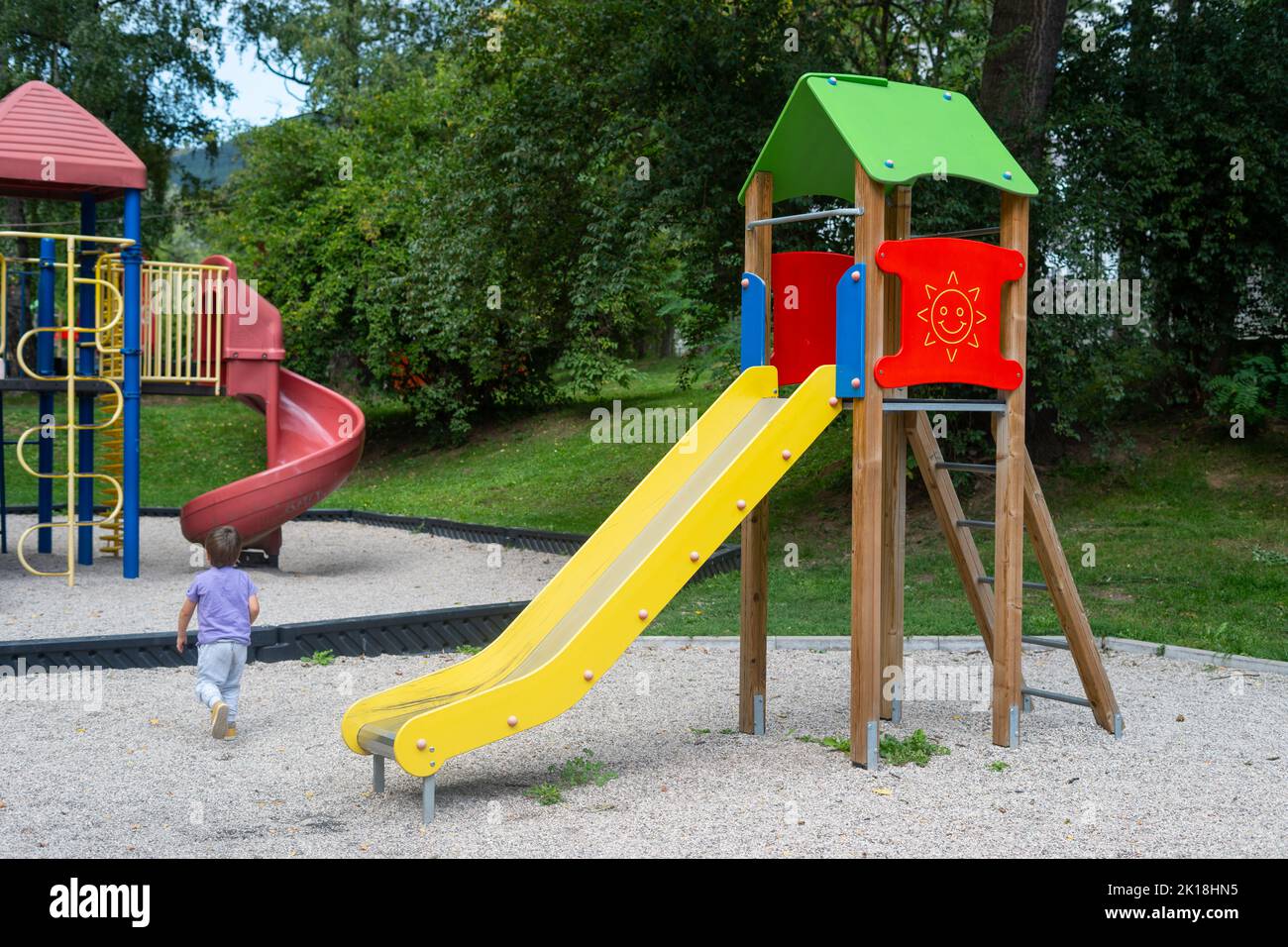 Un enfant (garçon) (non reconnaissable) qui court et joue à côté du toboggan dans le parc de l'aire de jeux pour enfants Banque D'Images