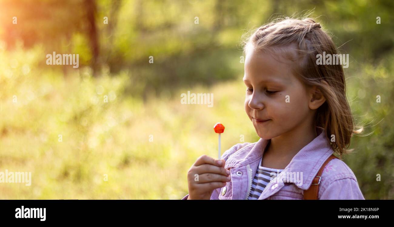 une petite fille dans la nature avec un lollipop dans ses mains est souriante et regarde la caméra Banque D'Images