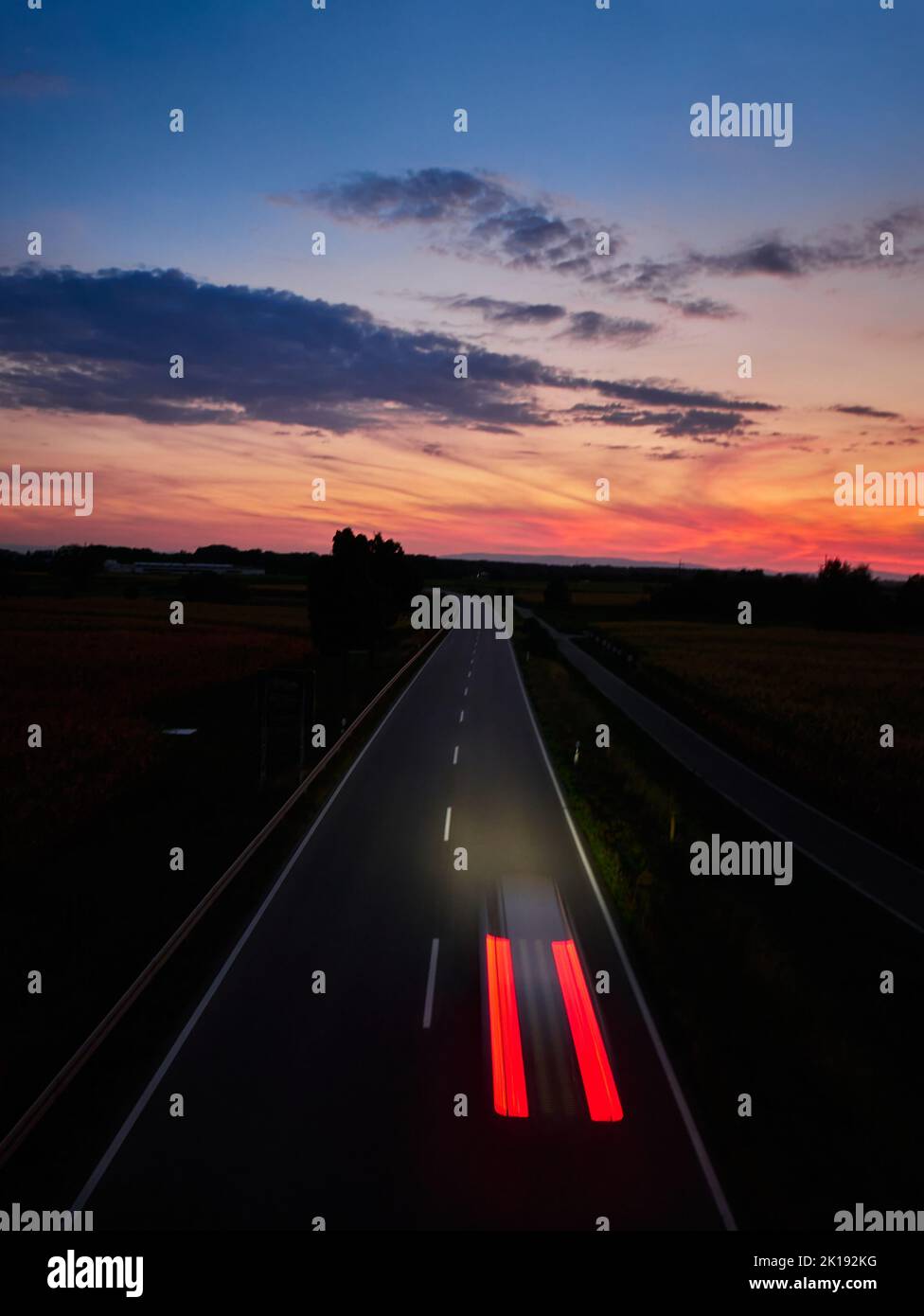 Un paysage spectaculaire d'un coucher de soleil vibrant dans le ciel avec une voiture roulant sur une route asphaltée Banque D'Images