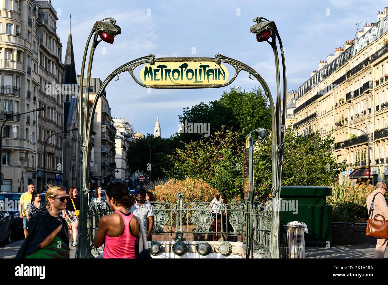 Panneau avec le logo du métro (symbole jaune et vert) devant une station de métro parisienne (Metropolitain) avec un ciel bleu en arrière-plan pendant a s. Banque D'Images