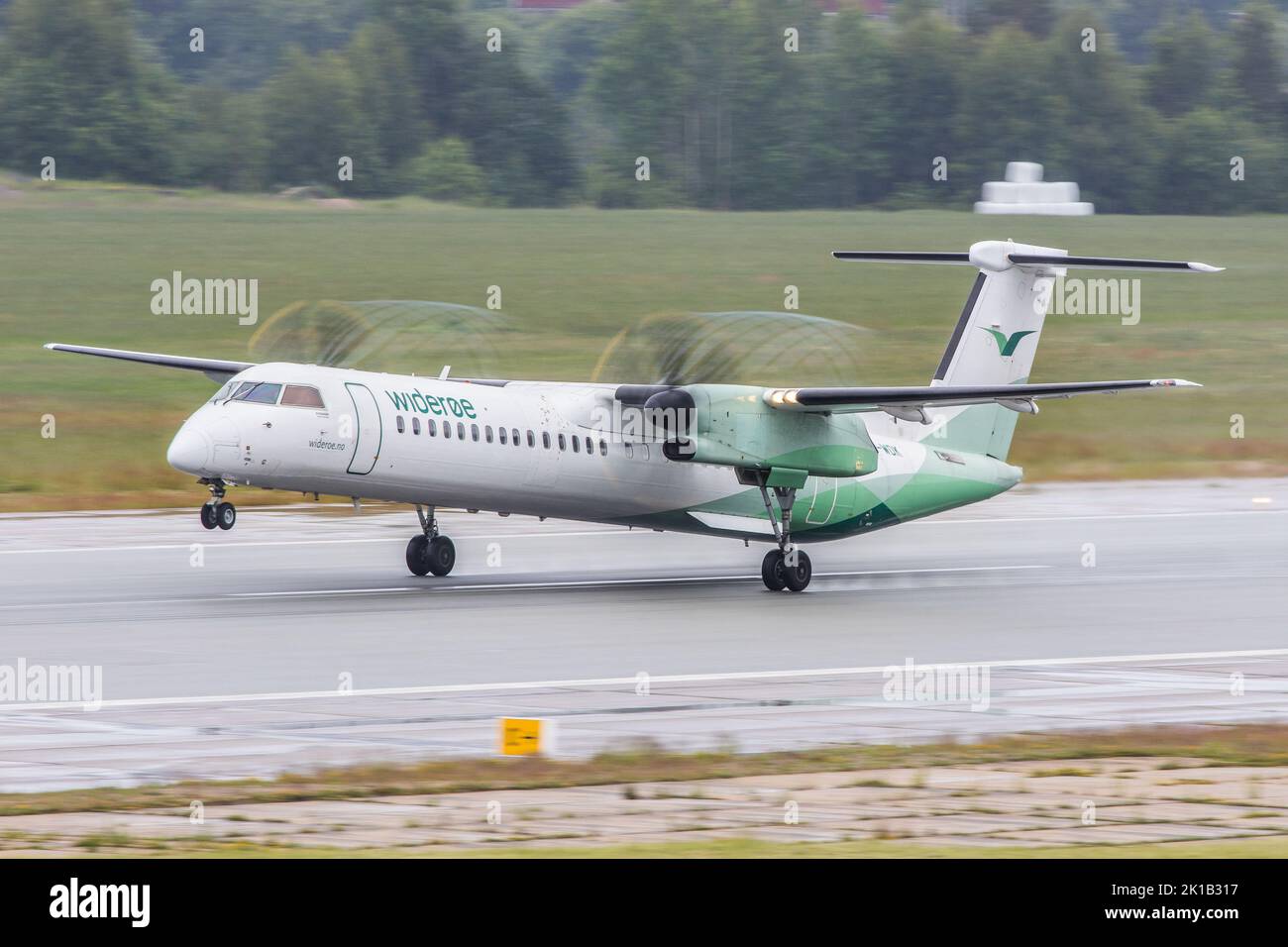 Un avion de ligne à turbopropulseur Dash 8 de Widerøe Airlines dévie sur une piste mouillée par temps pluvieux pour un vol à destination d'Oslo Banque D'Images