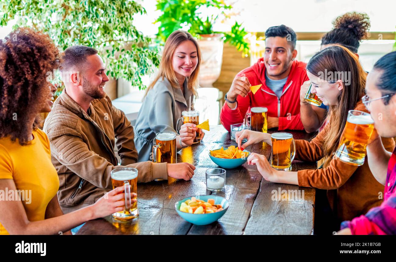 groupe d'amis célébrant l'happy hour en buvant des bières au bar-restaurant à l'intérieur, en s'amusant ensemble. des jeunes heureux assis sur une table de pub applaudissent Banque D'Images