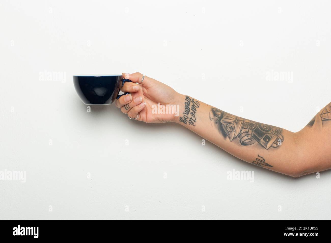Gros plan d'une main et d'un bras de femme tatoués avec une tasse de café sur fond blanc Banque D'Images