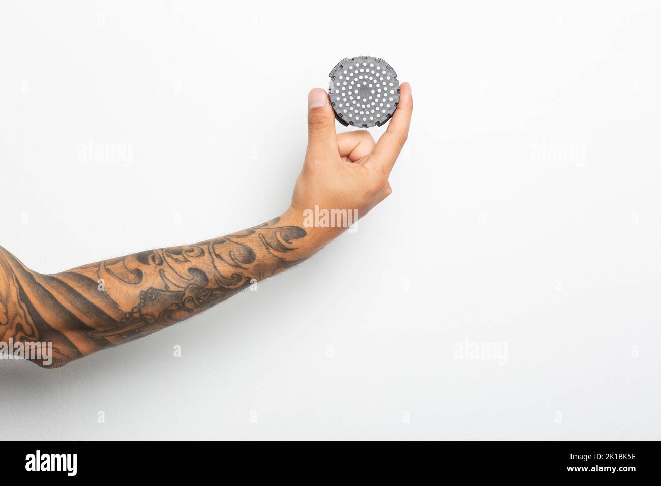 Main et bras d'un homme tatoué avec un capuchon de filtre d'aéropress isolé sur blanc Banque D'Images