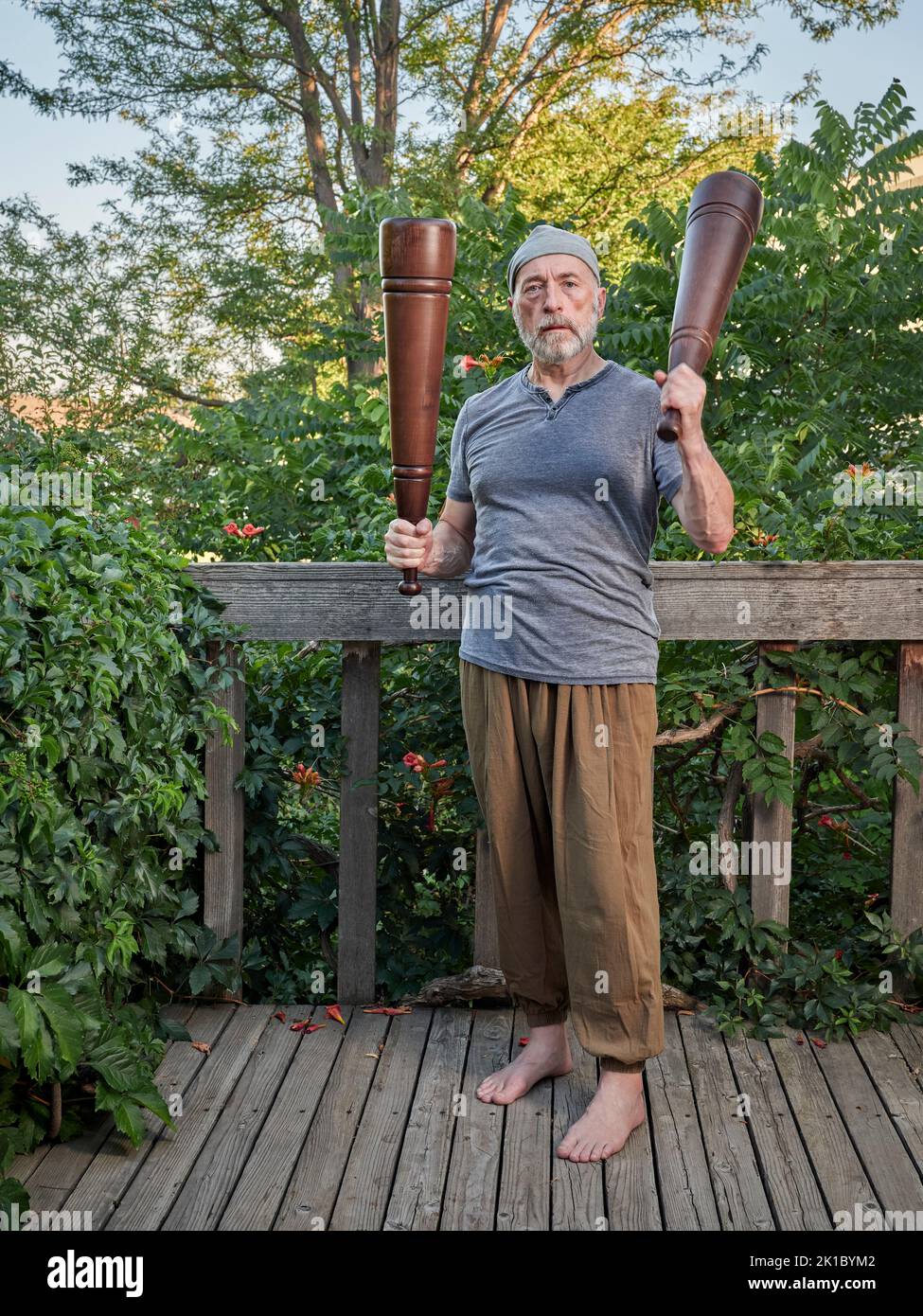 L'homme âgé (fin 60s) fait de l'exercice avec de lourds méels persans dans son patio d'arrière-cour, concept de forme physique fonctionnelle utilisant des outils traditionnels Banque D'Images