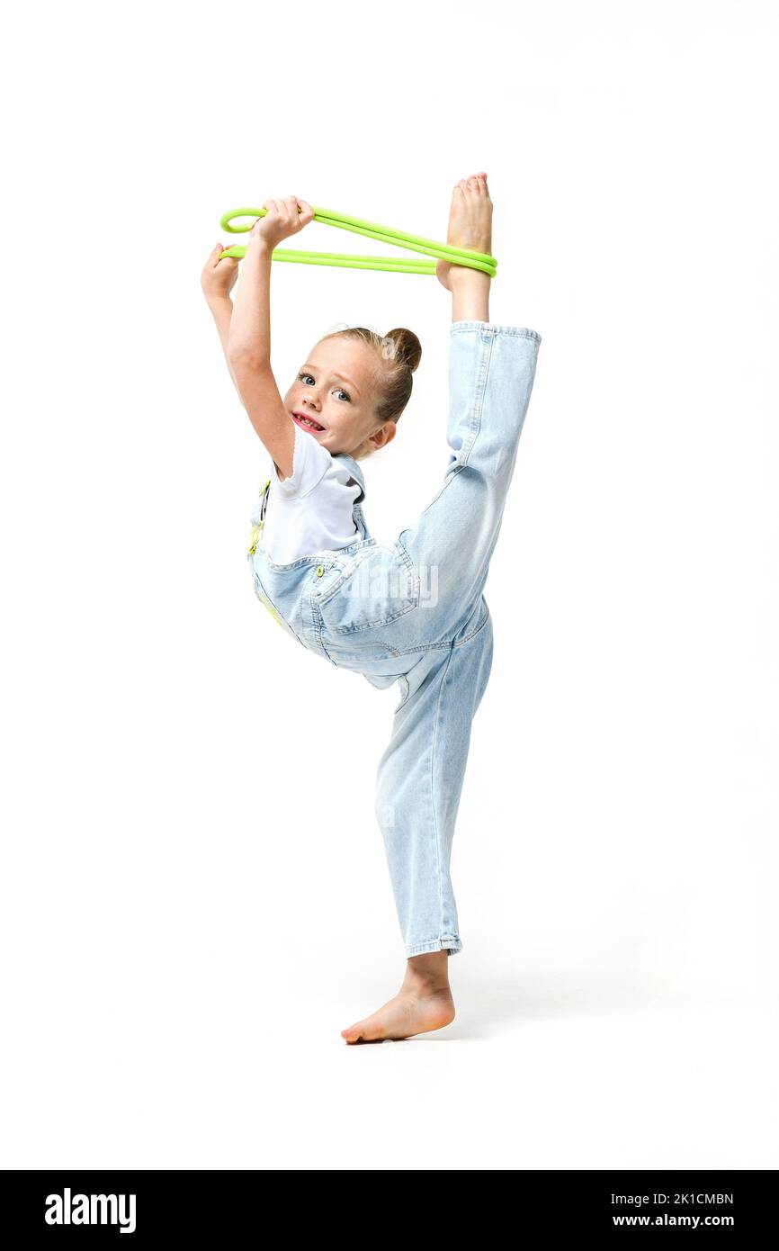 Flexible petite danseuse de gymnaste acrobat fille étirant le corps, mettre les pieds sur la tête. Petite fille vêtue de combinaisons en denim avec corde de saut. Banque D'Images