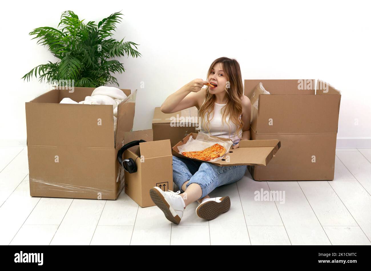 Une fille est assise parmi les boîtes et mange pizza.se déplaçant à une nouvelle maison Banque D'Images
