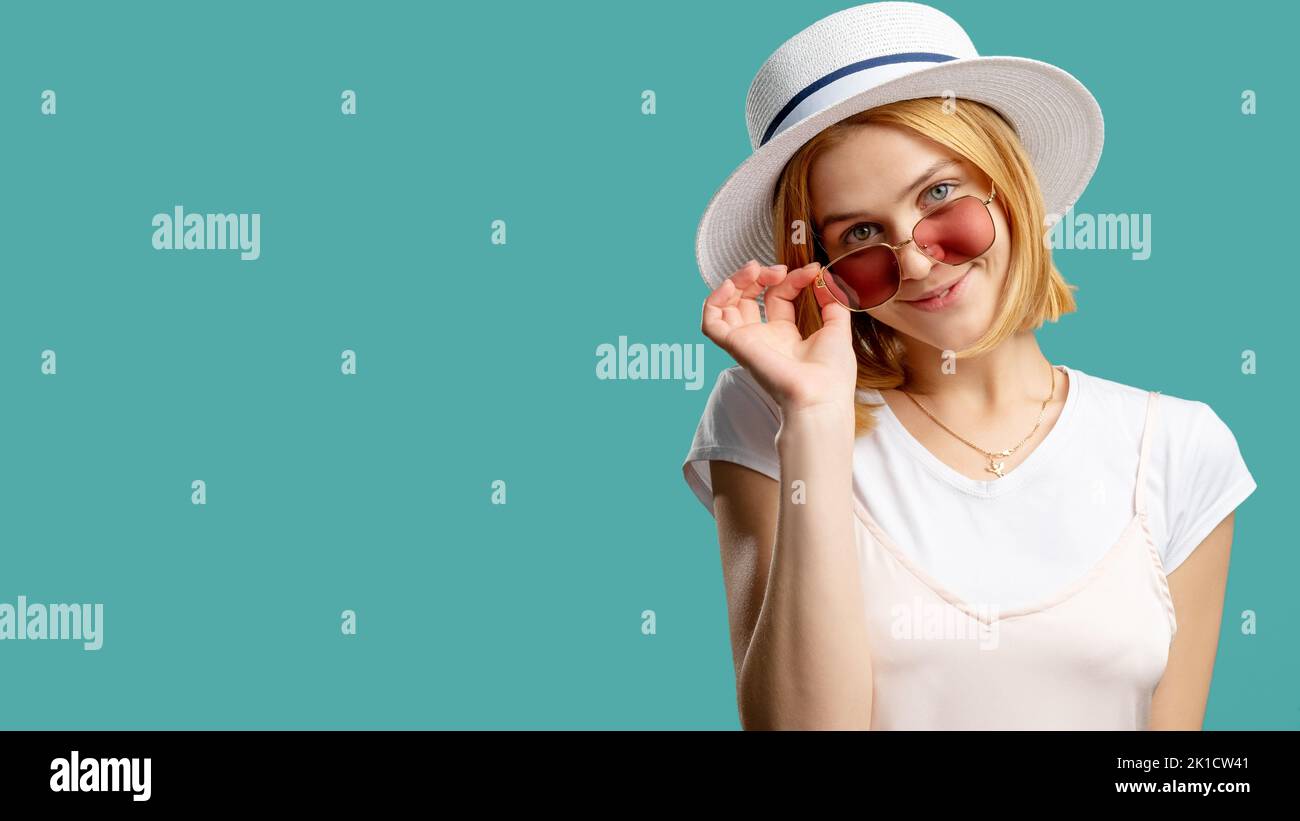 Accessoires d'été. Voyage de vacances. Bonne femme en tenue blanche chapeau tzigane regardant l'appareil photo sur des lunettes de soleil isolées sur l'espace de copie turquoise. Âge du voyage Banque D'Images